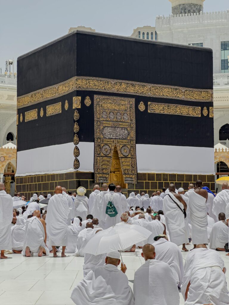 Pilgrims in white garments gather around the Kaaba in Mecca during daytime prayers.